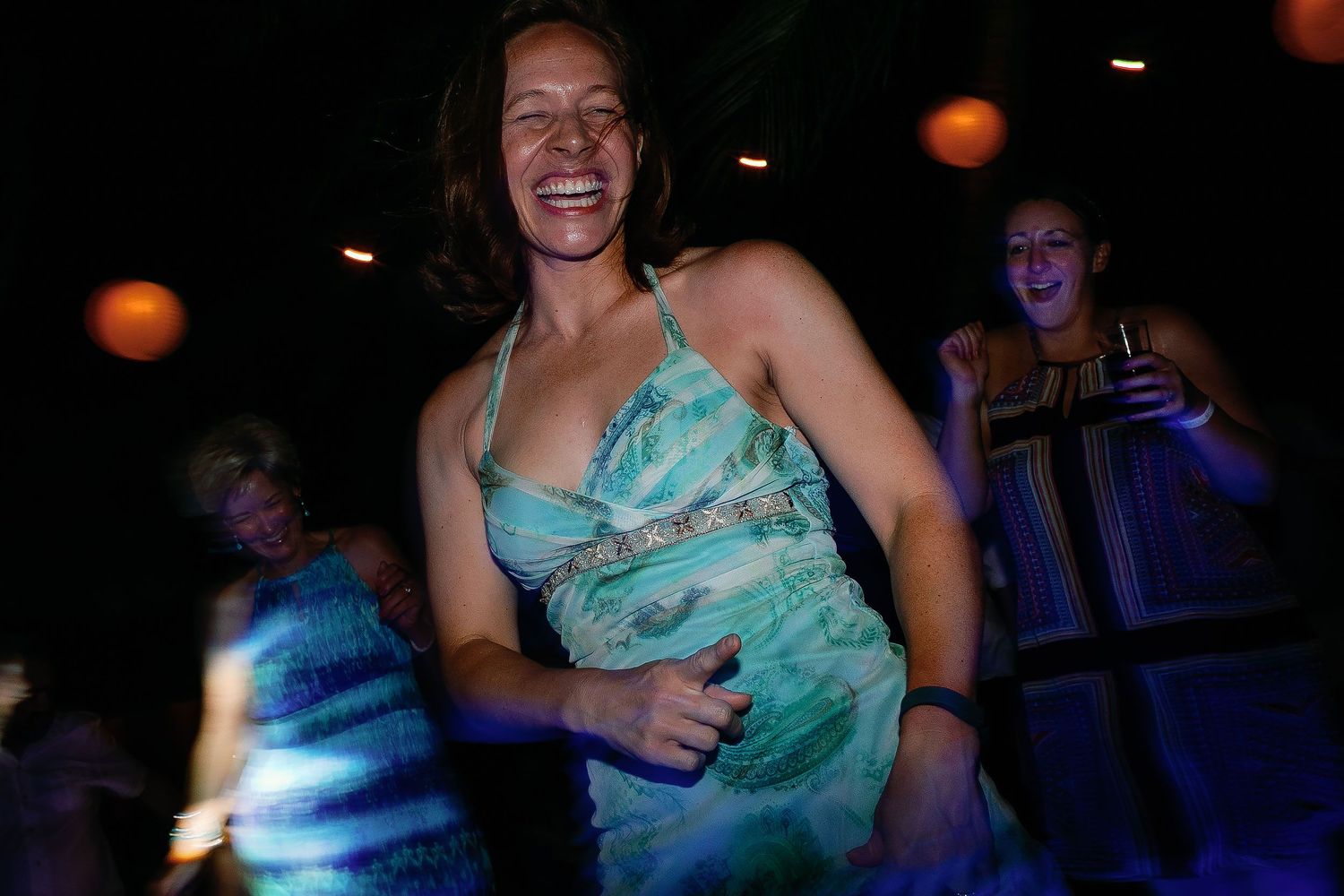 A laughing guest dances in a turquoise dress as friends celebrate behind her.