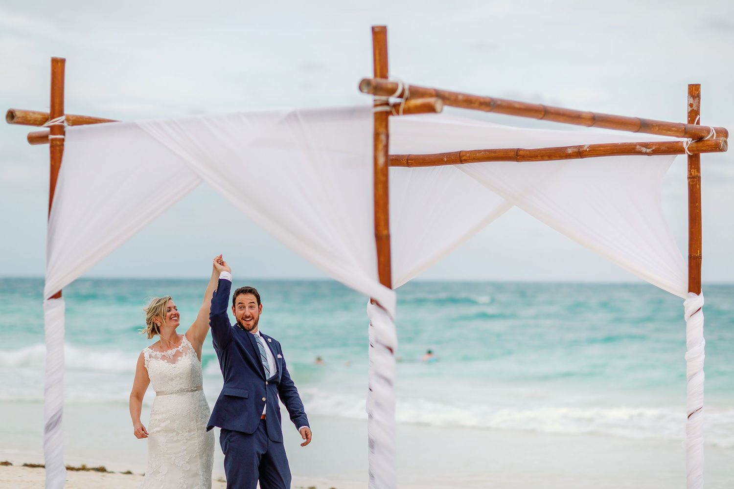 Ashley and Matt raise their joined hands beneath a white canopy after their Tulum beach ceremony.