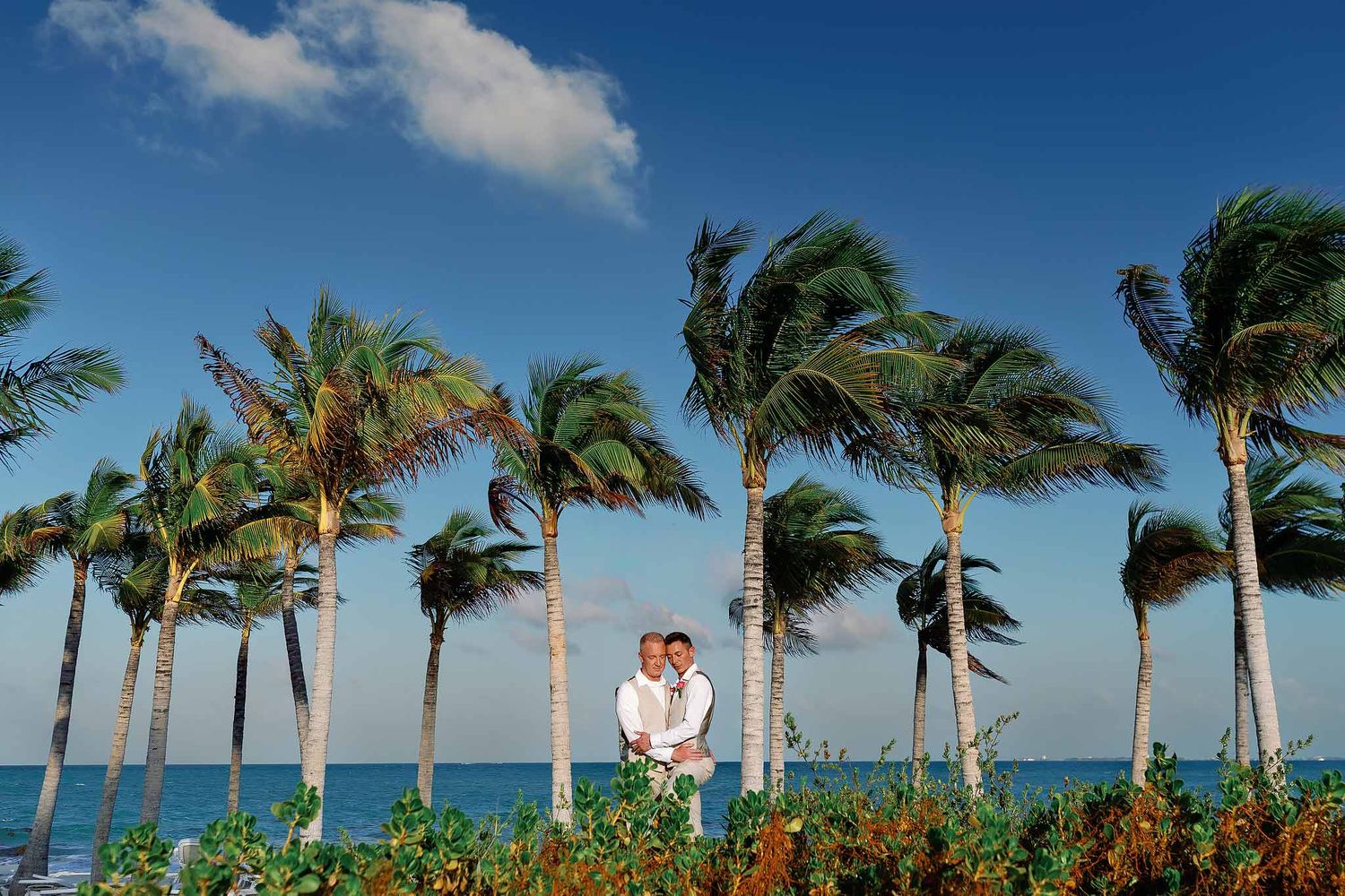 Elegant gay wedding portrait in Cancun surrounded by palm trees and Caribbean views at a luxury destination beach wedding