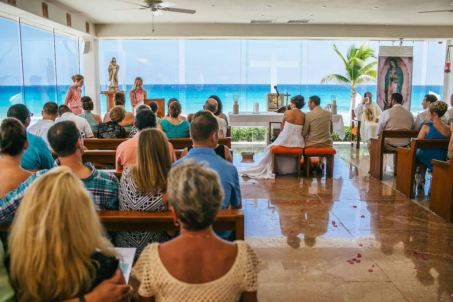 Catholic wedding ceremony at Sunscape Cancun chapel with bride and groom at altar overlooking ocean and guests seated