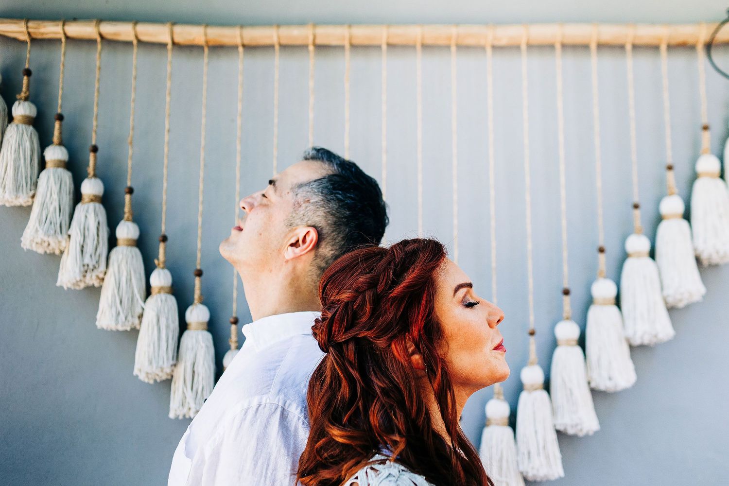 Sarah and Evish lean back to back beneath hanging tassels at their Tulum elopement.