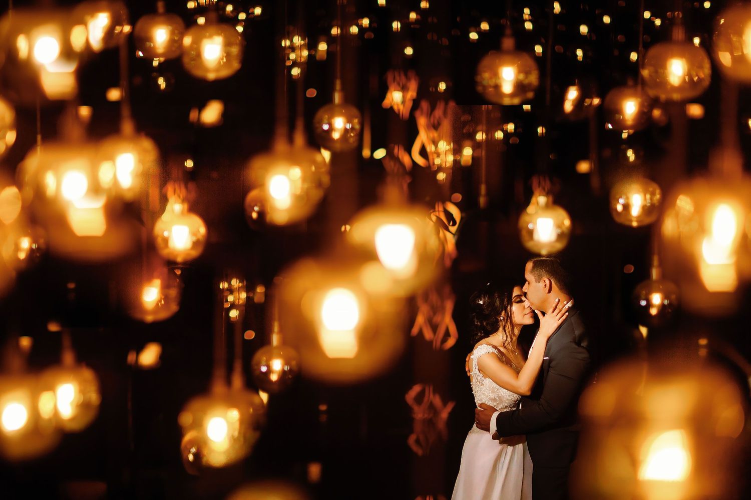 Bride and groom embracing beneath warm hanging lights during their creative wedding portrait session at Royalton Riviera Cancun.