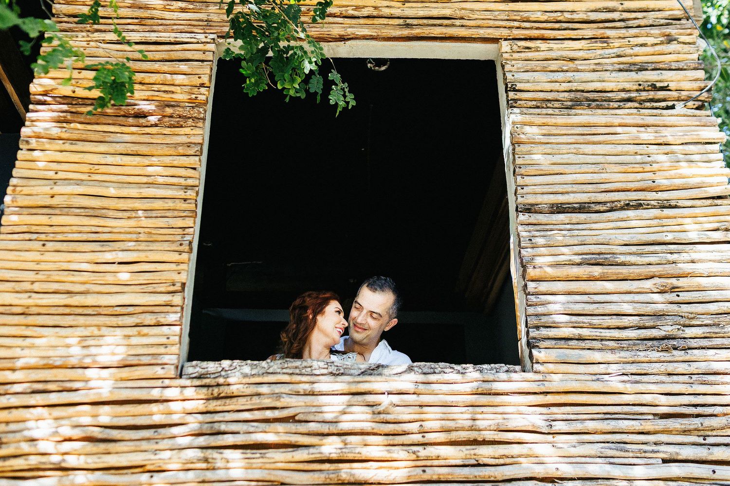 Sarah and Evish smile together through a rustic wooden window in Tulum.