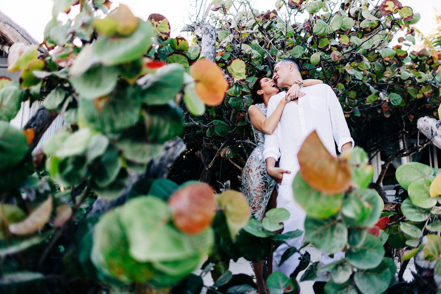 Sarah and Evish laugh together among sea grape leaves in Tulum.