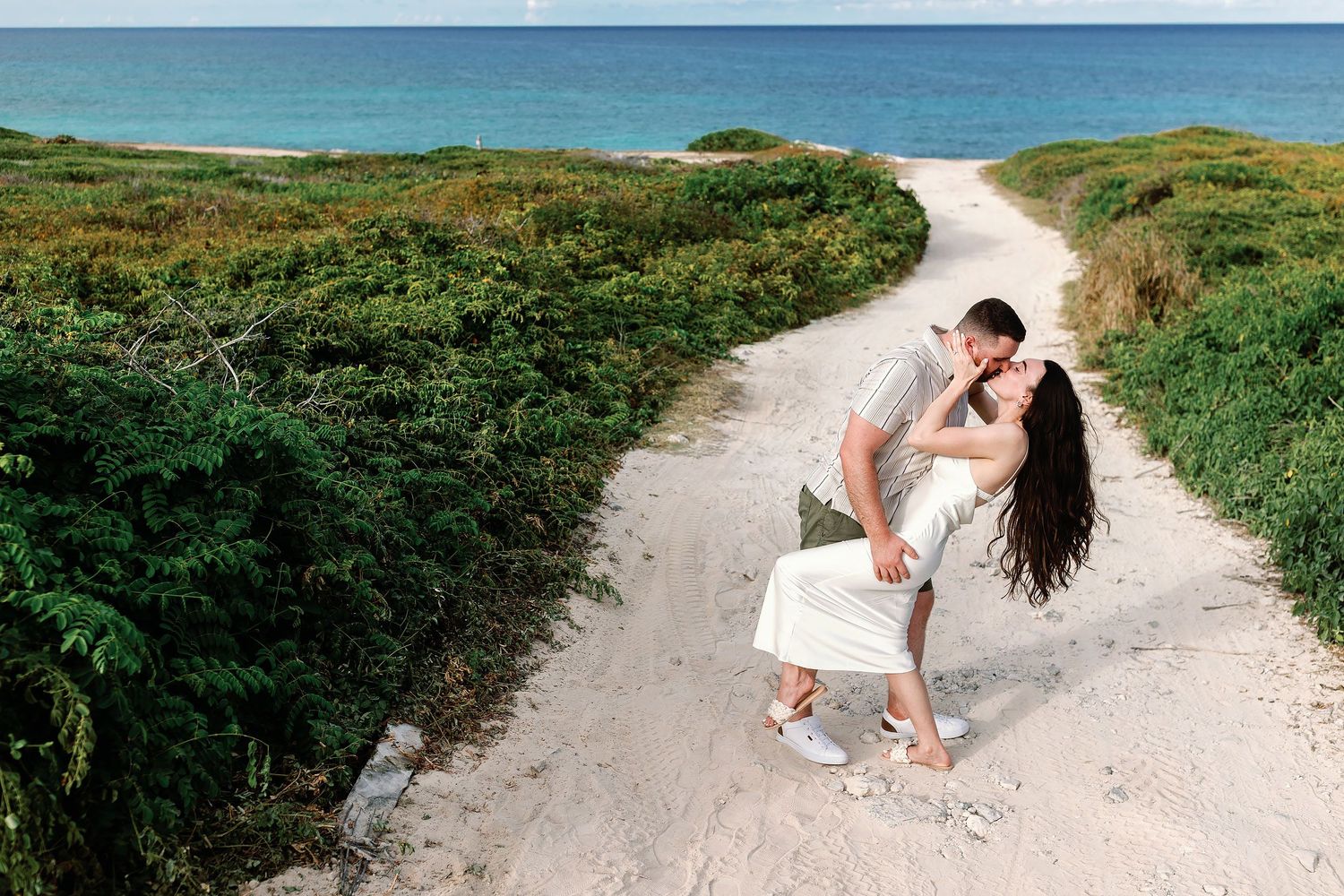 Alexia and Sam kiss on a sandy path leading toward the Caribbean Sea in Isla Mujeres.