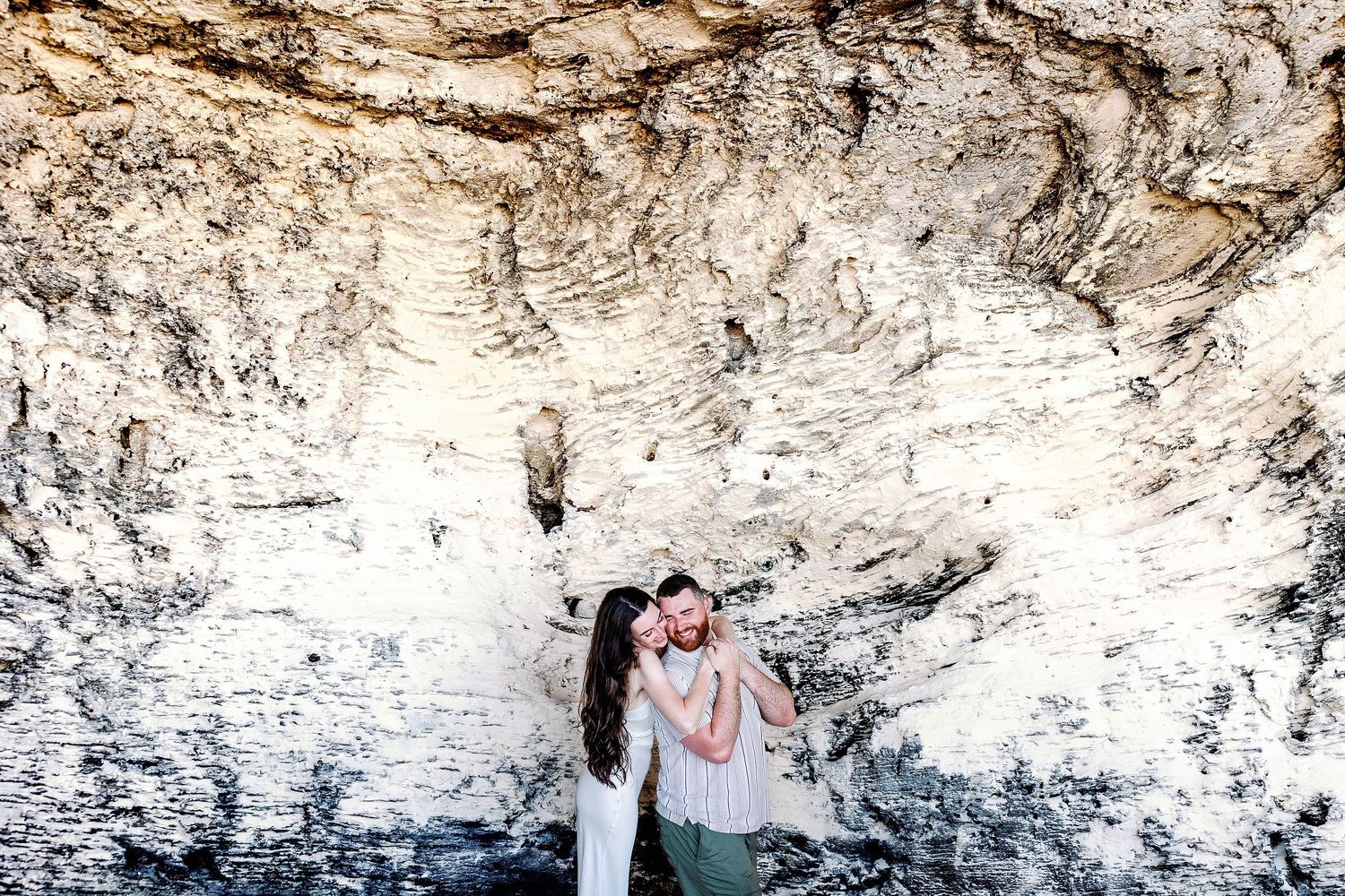 Alexia hugs Sam from behind against the textured limestone at Punta Sur.