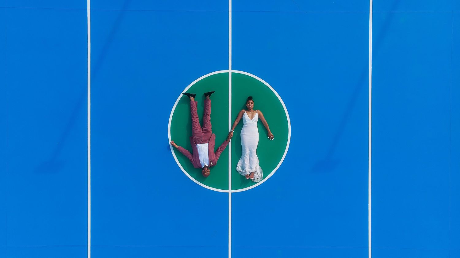 Bride and groom lying on a colorful sports court at Hard Rock Los Cabos captured by drone during a destination wedding photography session.