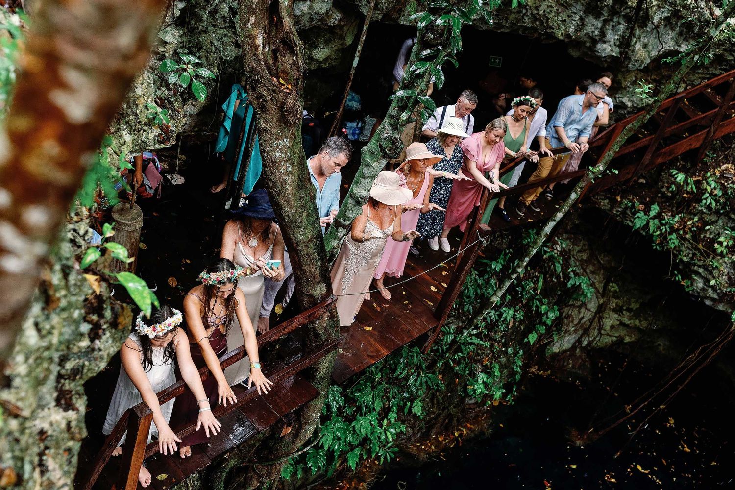 Wedding guests extending their hands during a Maya blessing beside the water at Cenote Hats’uts near Playa del Carmen.