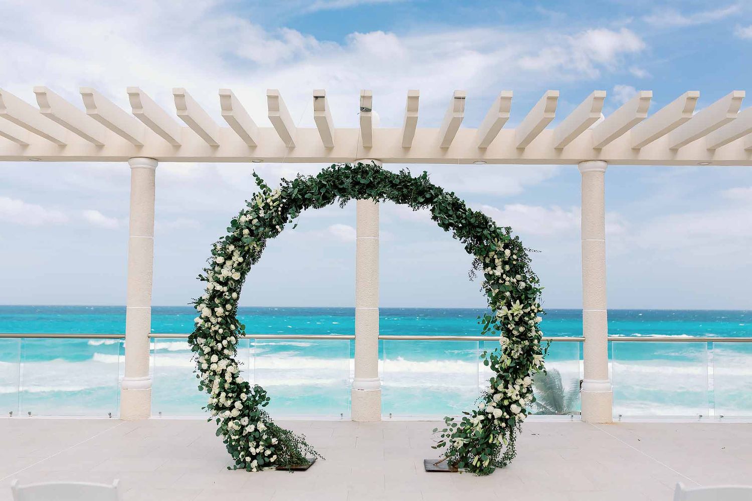 Luxury Cancun wedding ceremony setup with floral arch overlooking the turquoise Caribbean Sea at an oceanfront resort venue.