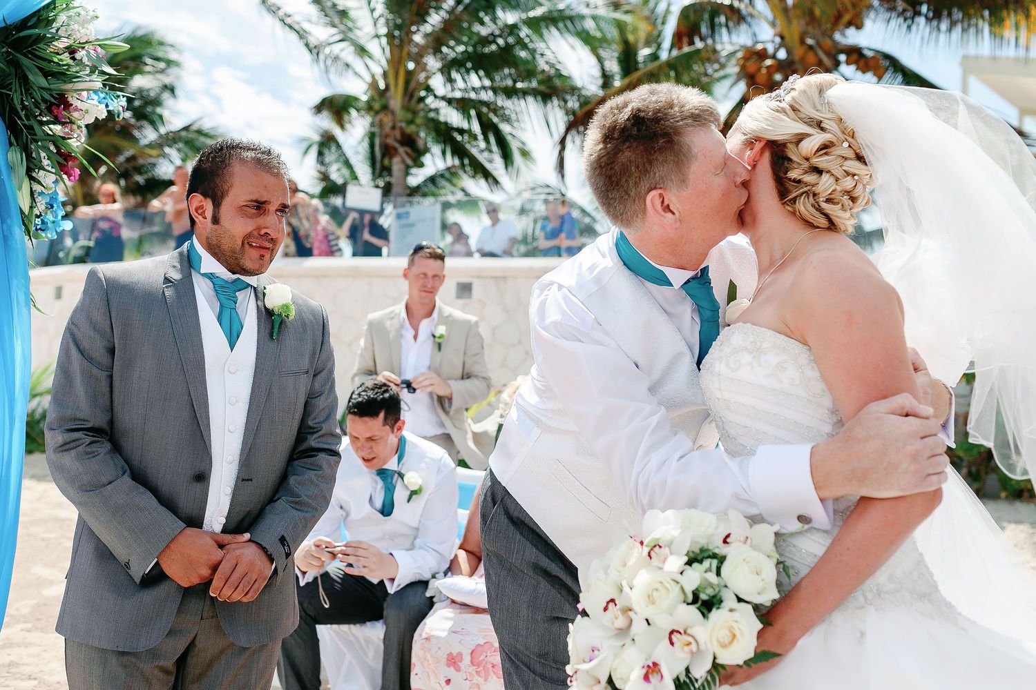 Bride receiving a kiss from her father after walking down the aisle while the groom looks on emotionally at Azul Beach Resort Riviera Cancun