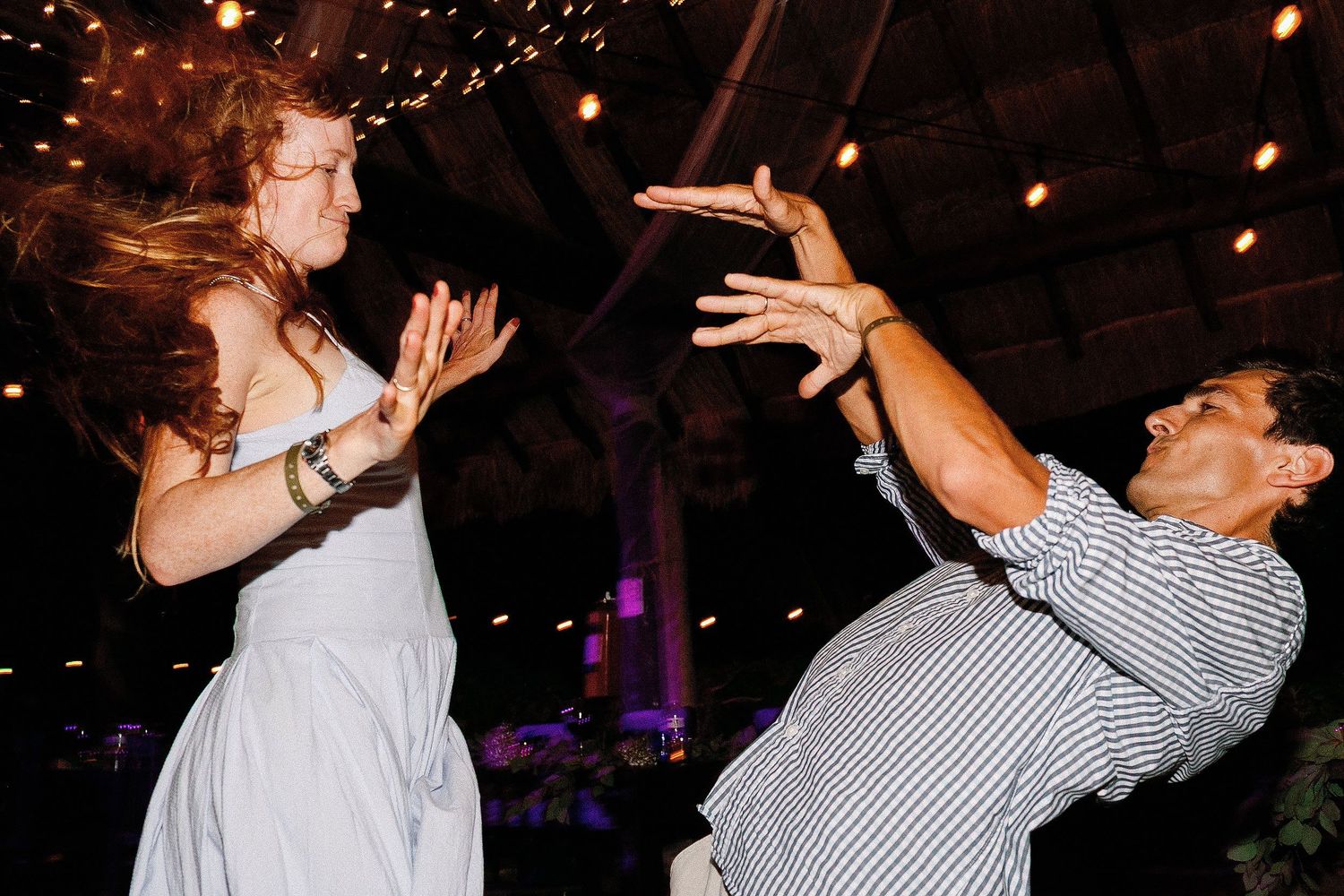 Two wedding guests laughing and dancing beneath the lights at Cressida and Alan’s Riviera Maya reception.