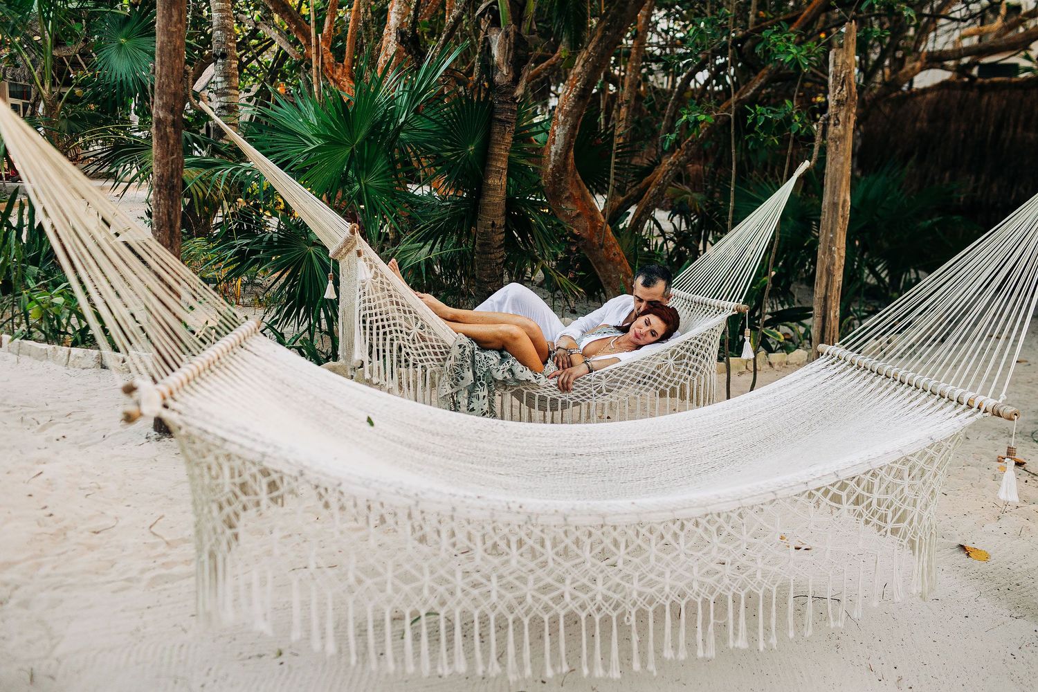 Sarah and Evish relax together in a woven hammock beneath tropical palms.