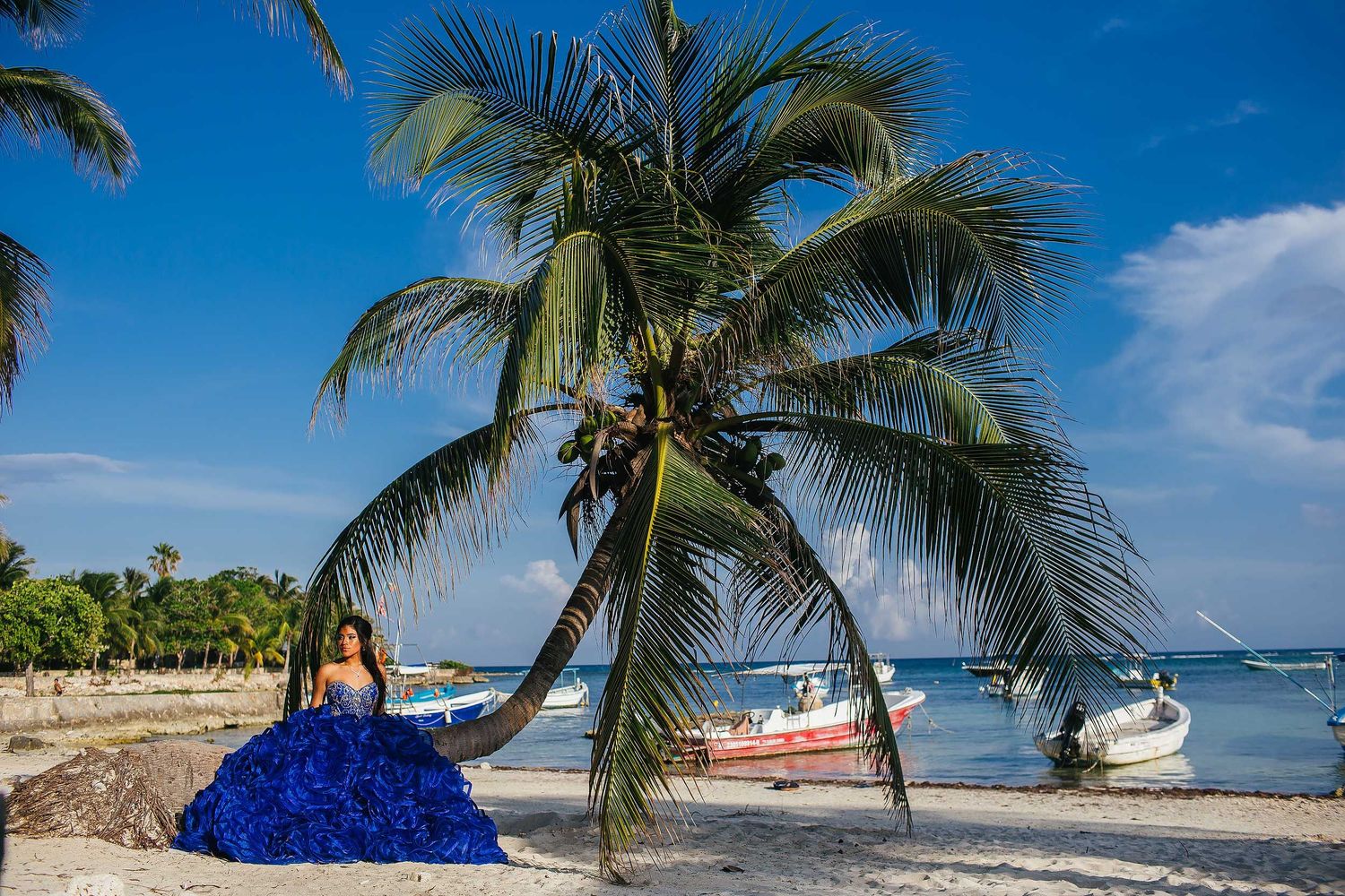 Sweet 15 portrait session in Akumal with a blue ball gown, tropical palm trees, boats, and turquoise Caribbean water.