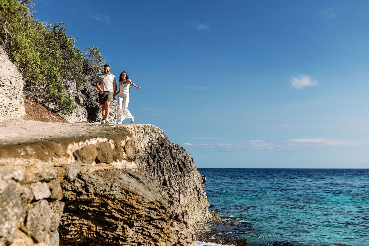 Alexia and Sam walk hand in hand along the rocky coast at Punta Sur in Isla Mujeres.