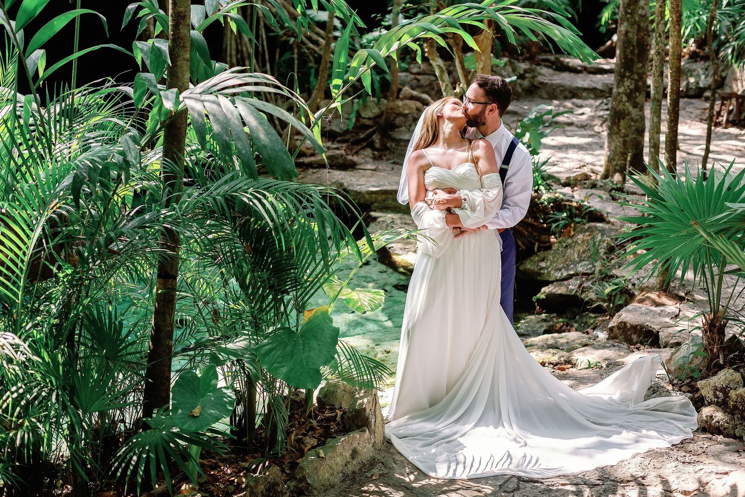 Nicole and Thomas kissing among tropical greenery before their underwater wedding photography session at Cenote Azul near Playa del Carmen.