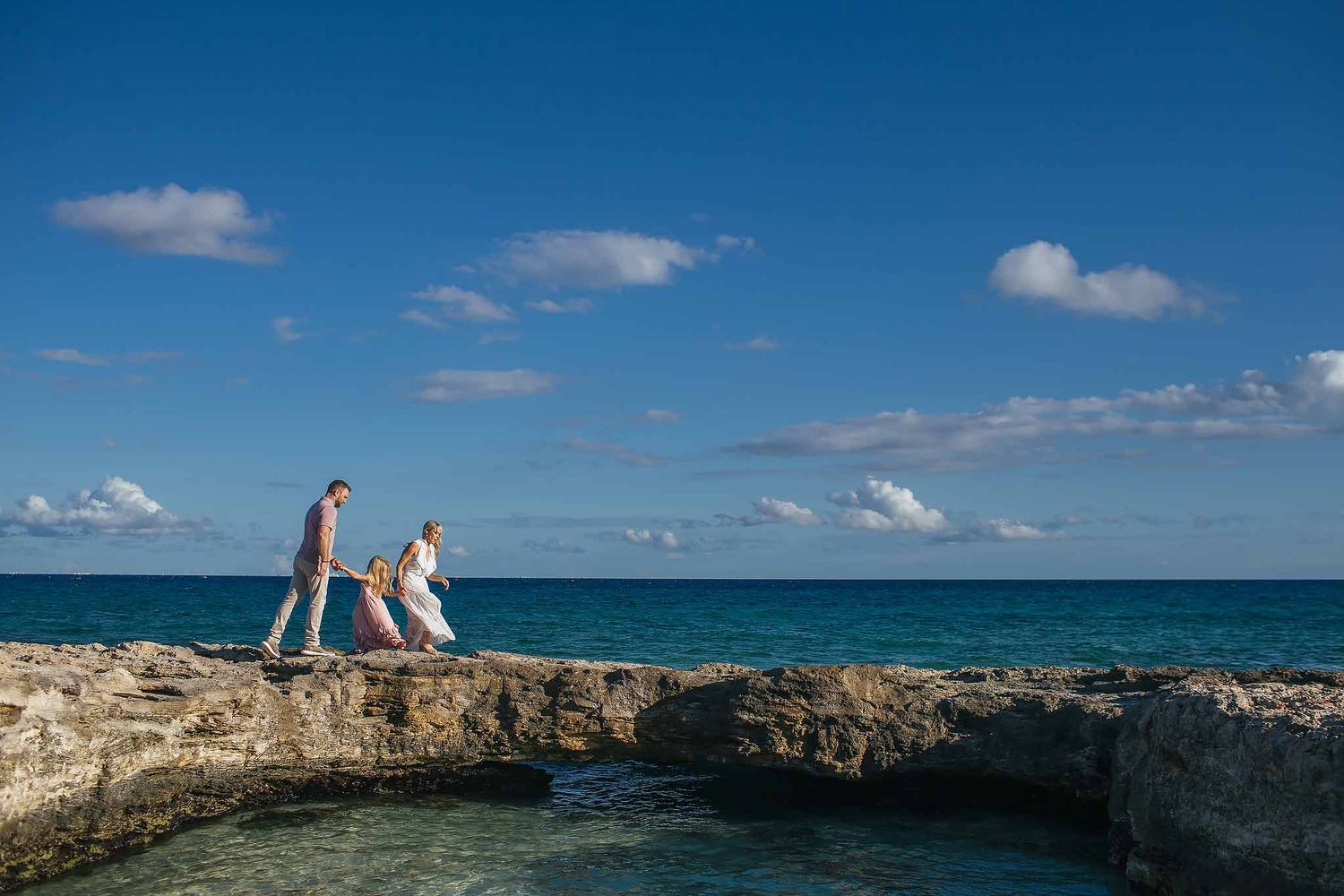 Family walking on rocky beach by the ocean in Cancun during a Riviera Maya family photography session under blue sky