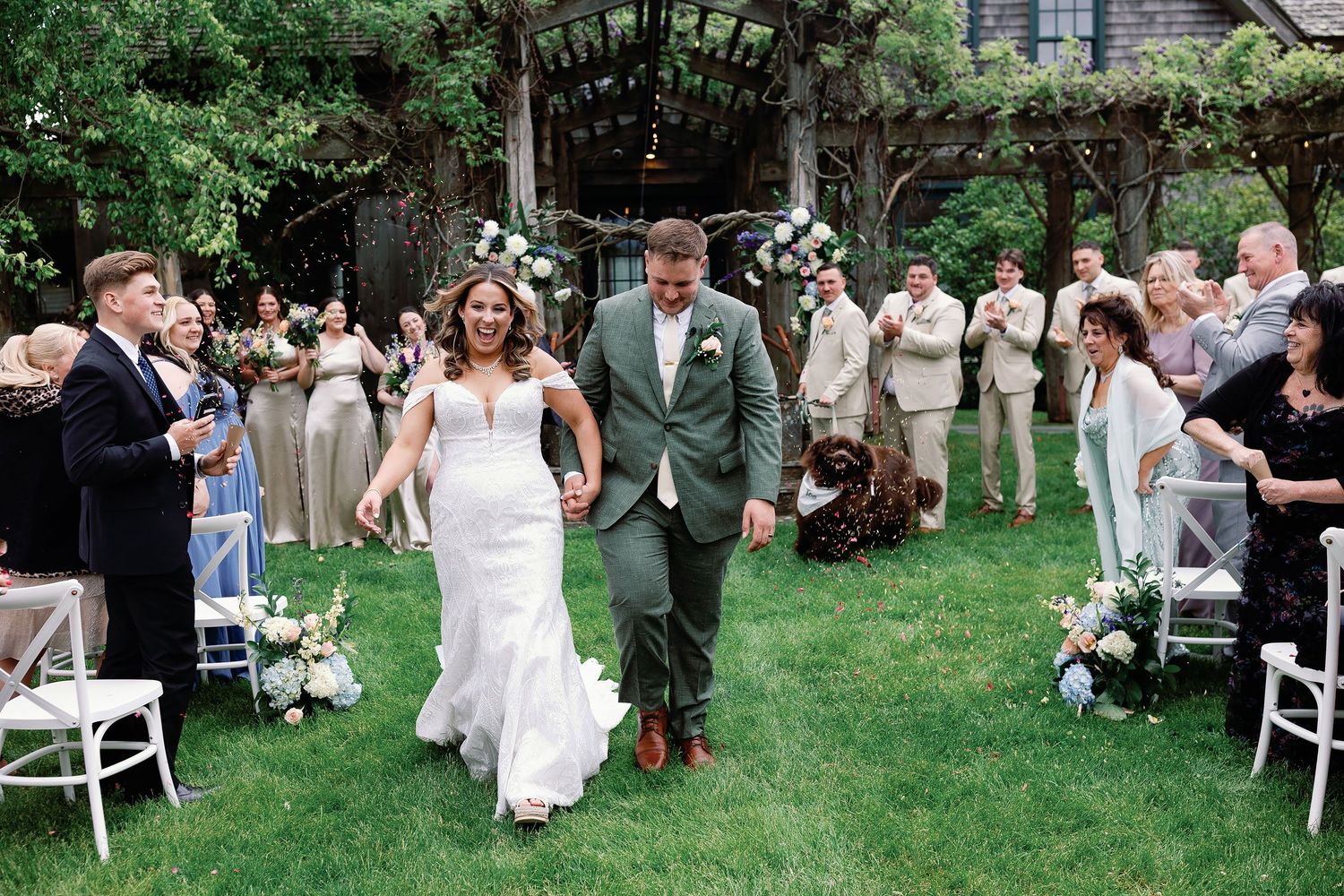 Jennifer and Collin walking hand in hand down a grassy aisle as guests cheer and toss confetti at their outdoor Minnesota wedding.