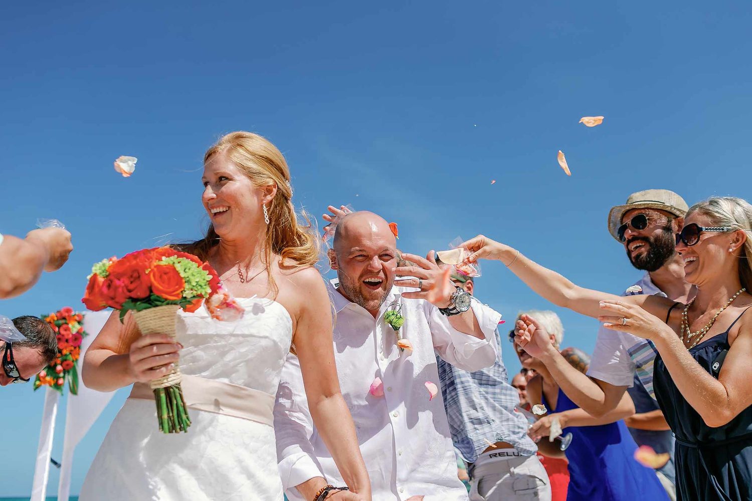 Bride and groom walking through guests throwing petals during beach wedding ceremony in Playa del Carmen