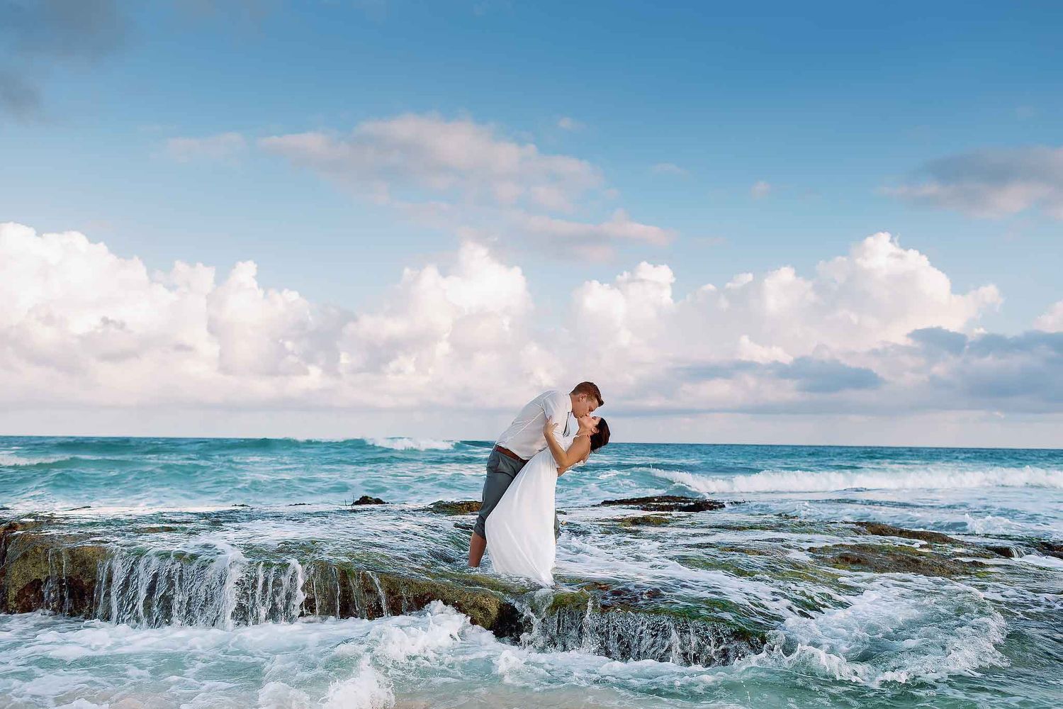 Romantic Isla Mujeres wedding couple kissing on ocean rocks with waves at sunset, destination wedding photography in Cancun Mexico