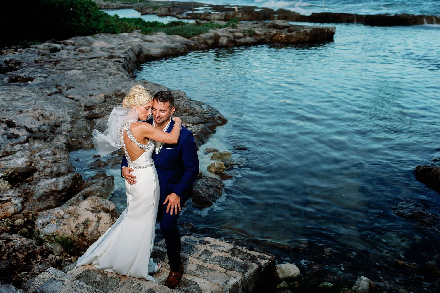 Bride and groom embracing along the rocky Caribbean shoreline during their wedding portrait session at Hard Rock Hotel Riviera Maya.
