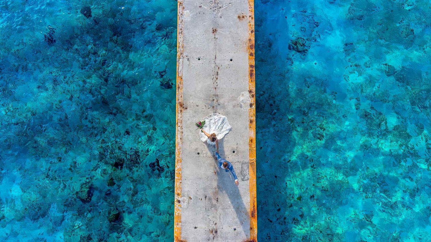 Bride and groom walking on a pier above turquoise water at InterContinental Presidente Cozumel Resort captured by a Cozumel wedding photogra