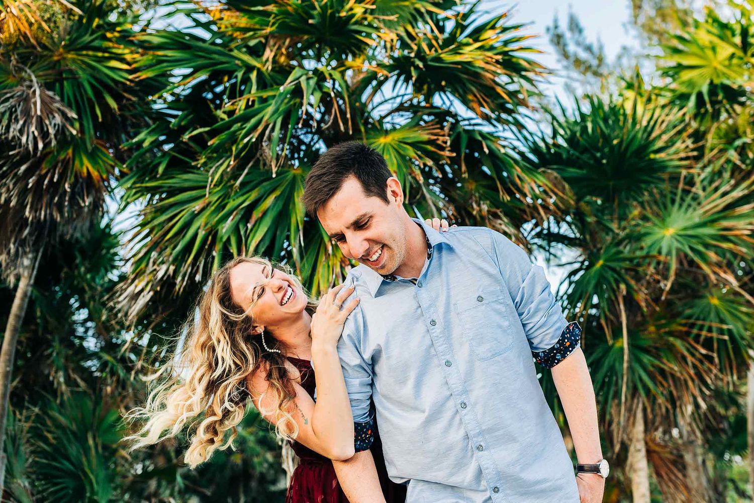 Happy engaged couple laughing together among tropical palms in Riviera Maya Mexico.