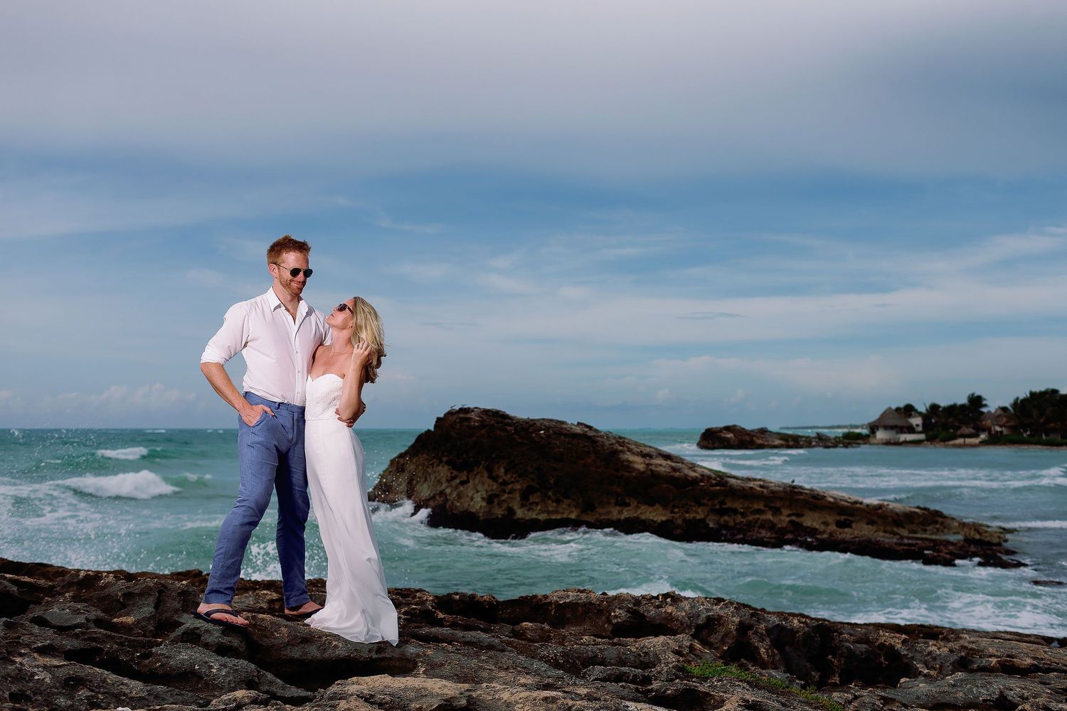 Cressida and Alan standing together on the rocky shoreline during their Tulum beach Trash the Dress session.