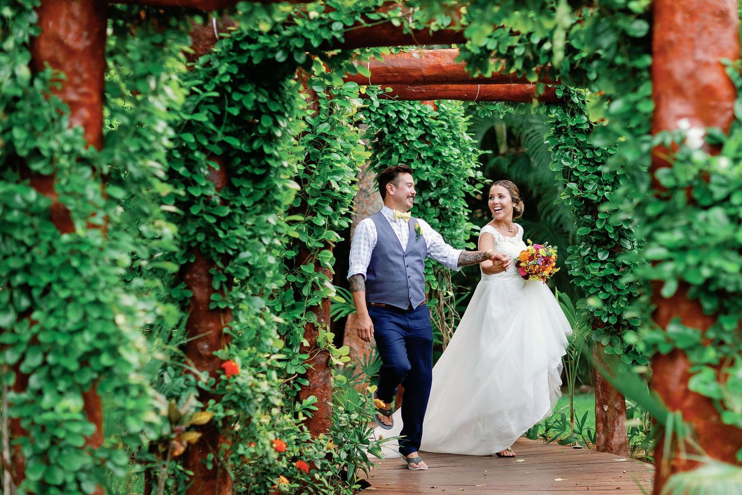 Bride and groom walking hand in hand through the tropical gardens at Sandos Playacar during their Playa del Carmen wedding portrait session