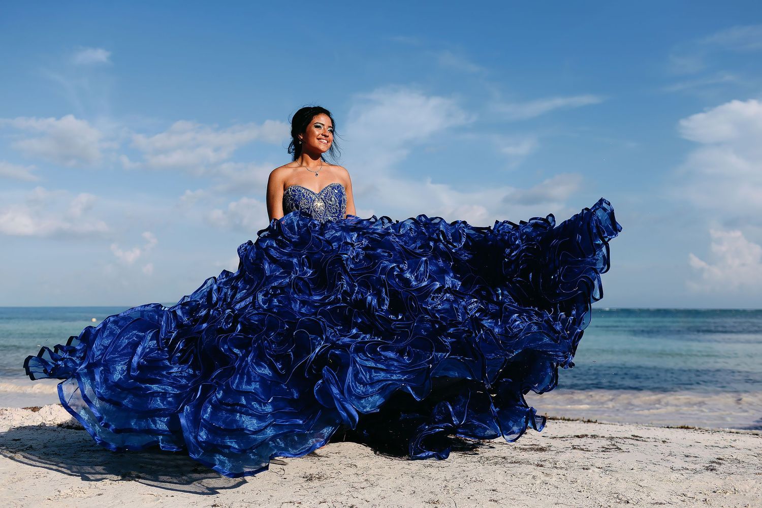 Quinceañera portrait in Isla Mujeres featuring a royal blue ball gown, Caribbean beach, and turquoise ocean backdrop.