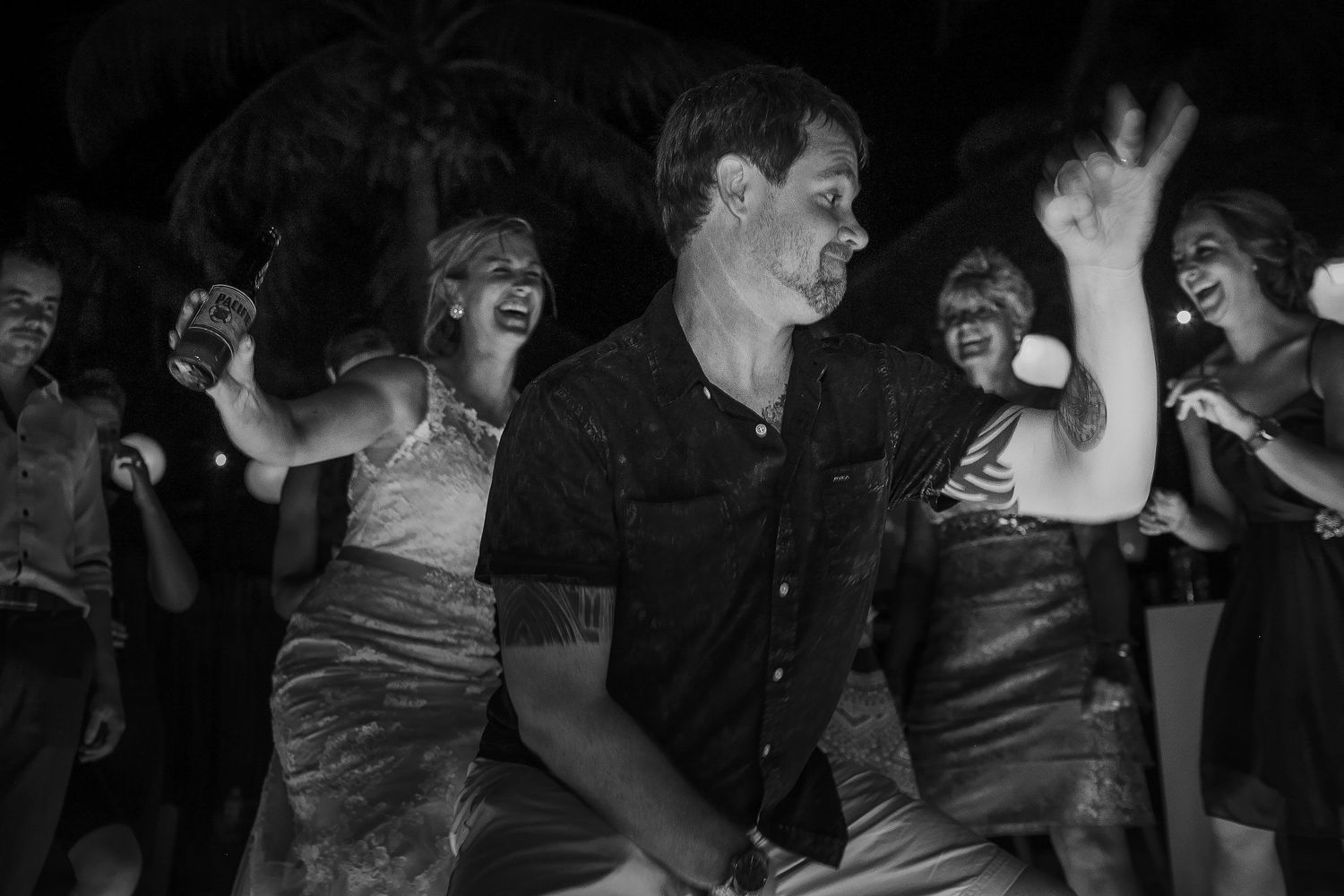 Black-and-white photograph of a guest dancing as Ashley and friends laugh behind him.