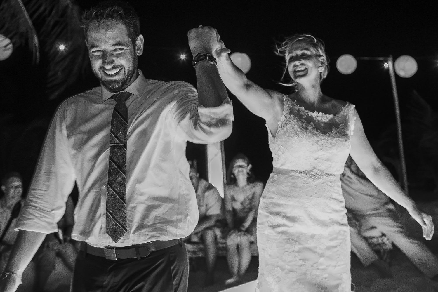 Black-and-white photograph of Ashley and Matt dancing hand in hand at their Tulum reception.