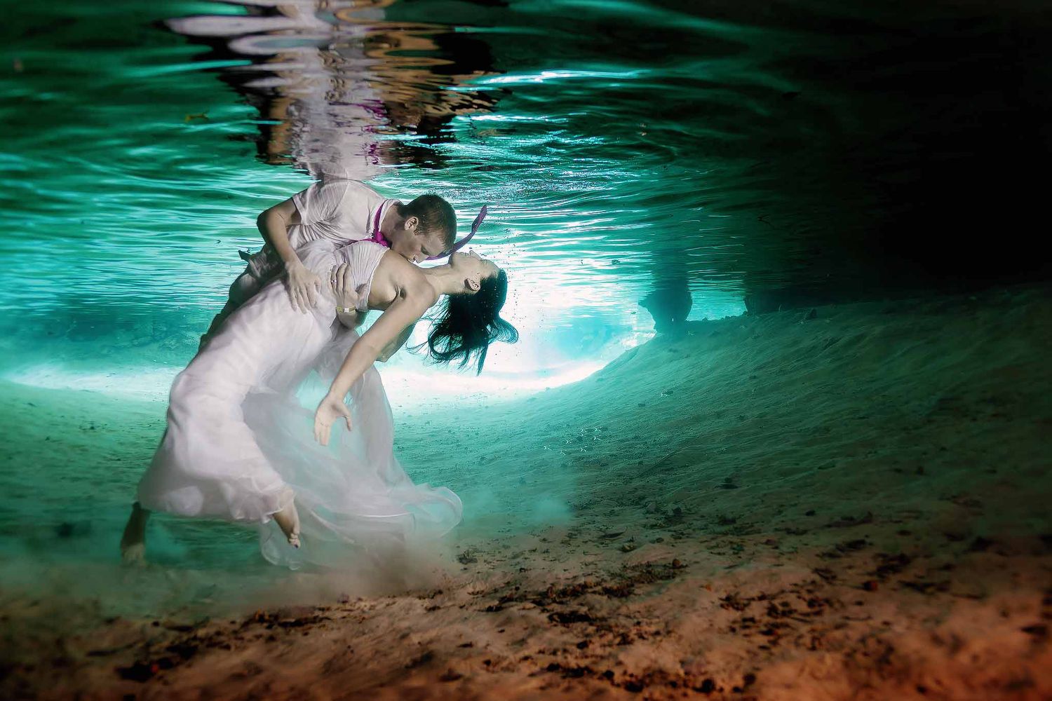 Romantic underwater wedding portrait in a Tulum cenote featuring a bride and groom embracing beneath crystal-clear water.
