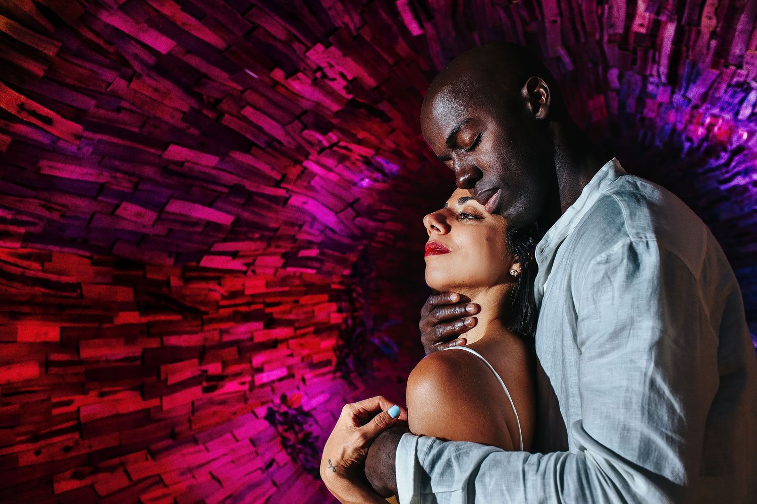 ania and Francoa embracing beside a textured wall illuminated with red and purple light during their Minneapolis portrait session.