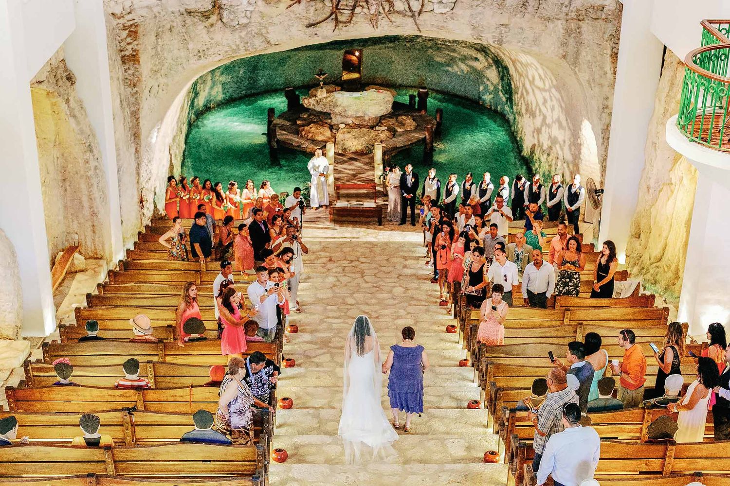 Bride walking down aisle inside Guadalupe Chapel cenote at Xcaret Park, Catholic wedding ceremony in Riviera Maya