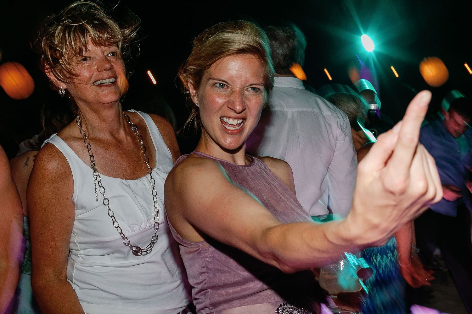 Two wedding guests gesture playfully toward the camera on the colorful beach-club dance floor.
