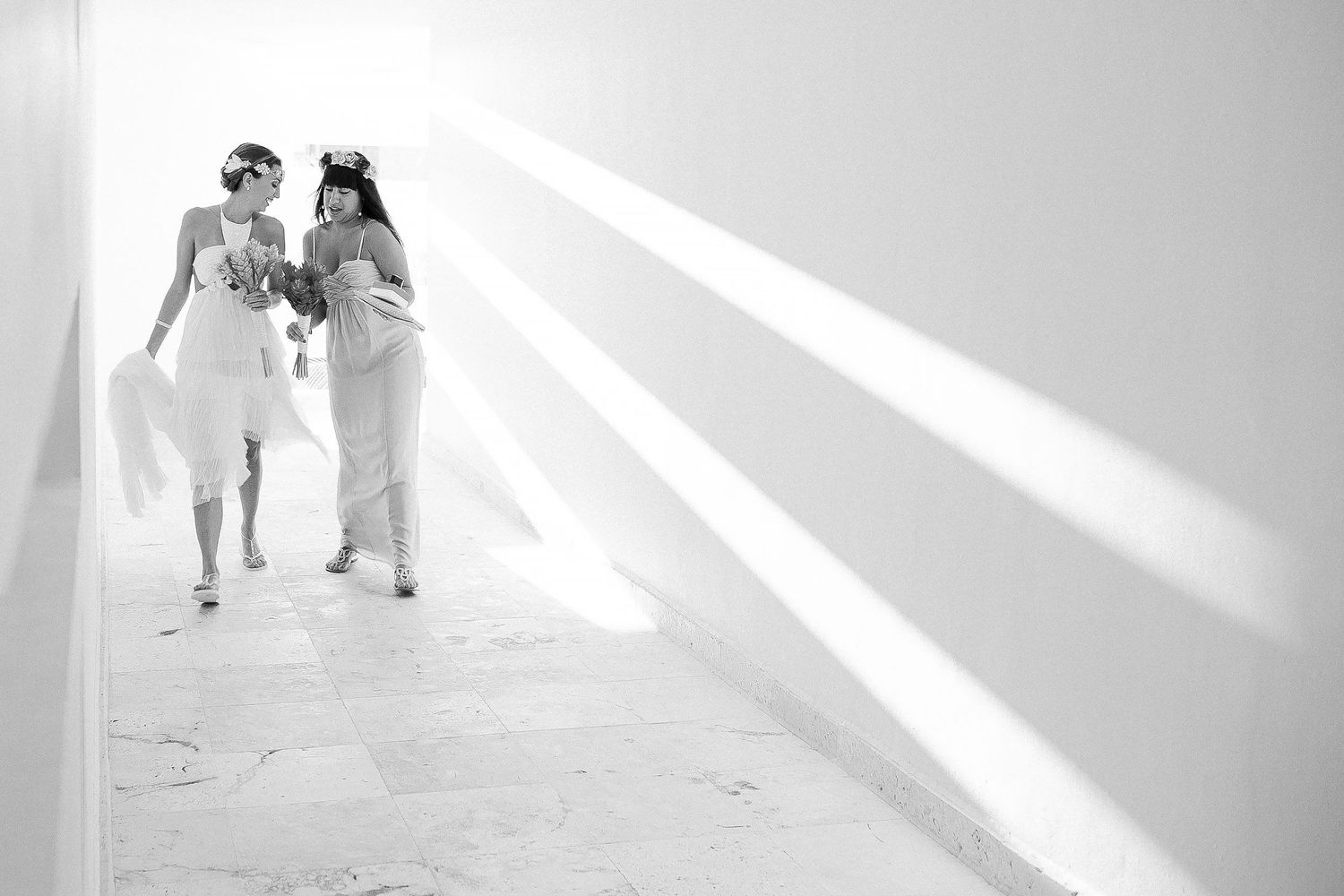 Juliana and a bridesmaid walk toward the beach ceremony carrying tropical bouquets.