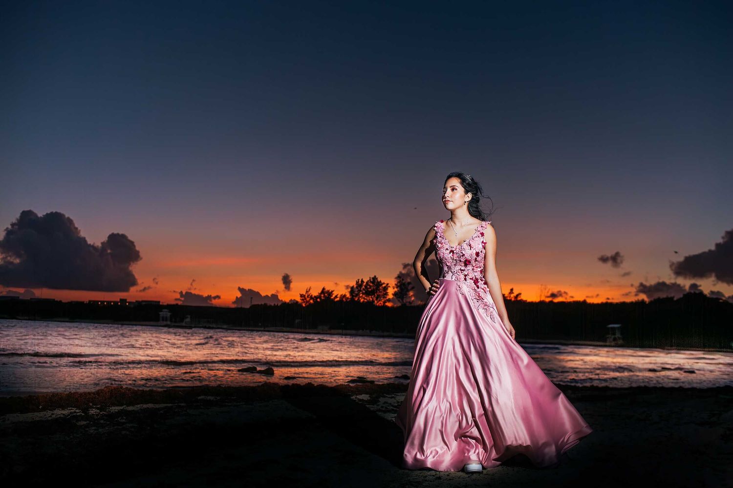 Quinceañera portrait in Puerto Vallarta featuring a pink gown, dramatic sunset sky, and coastal scenery at twilight.