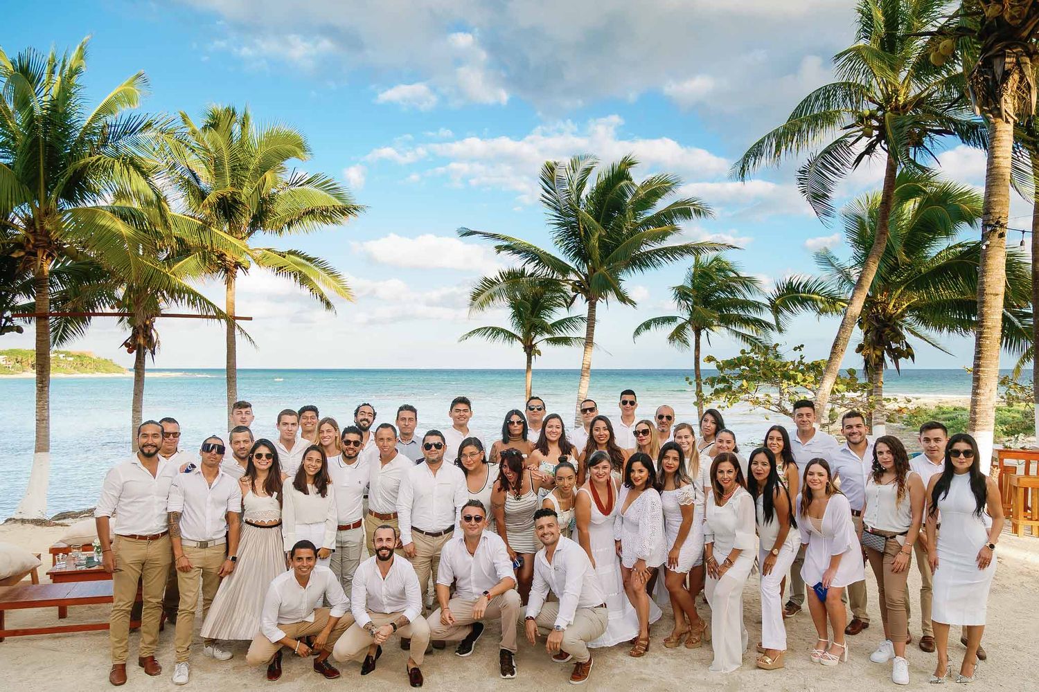 Corporate event photography Cancun featuring large team group photo on beach with palm trees and ocean background
