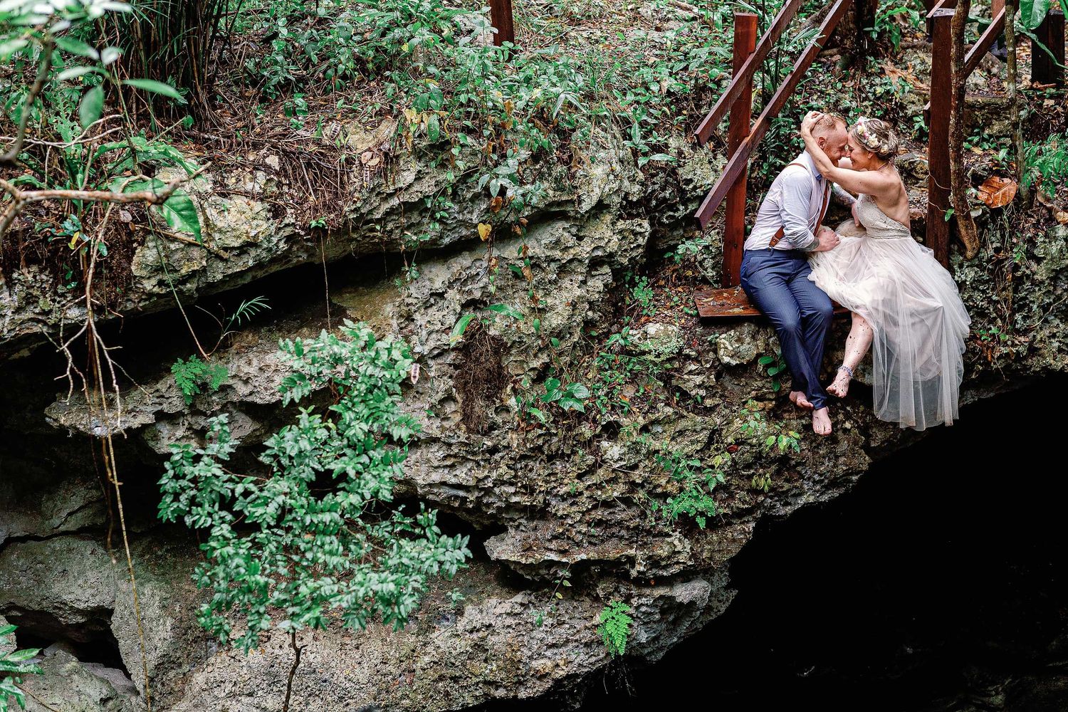 Jeff and Veronica sharing a kiss on a limestone ledge during their wedding portraits at Cenote Hats’uts near Playa del Carmen.