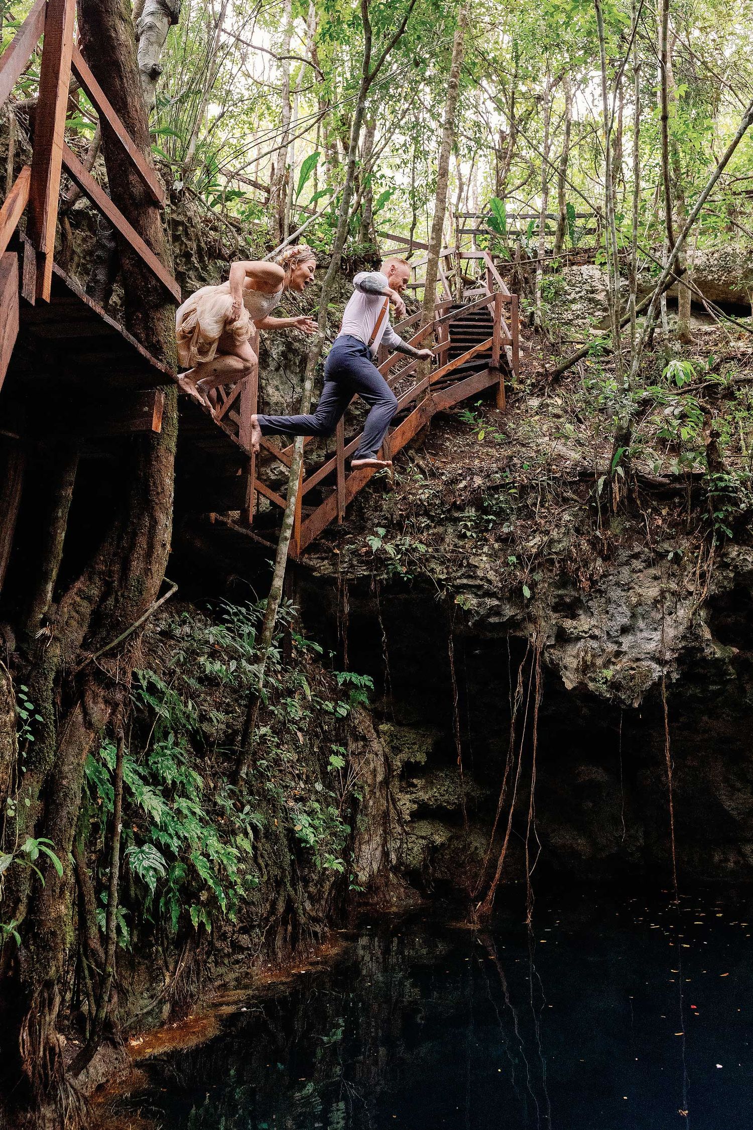 Jeff and Veronica jumping together from a wooden platform into the water at Cenote Hats’uts after their intimate Playa del Carmen wedding.