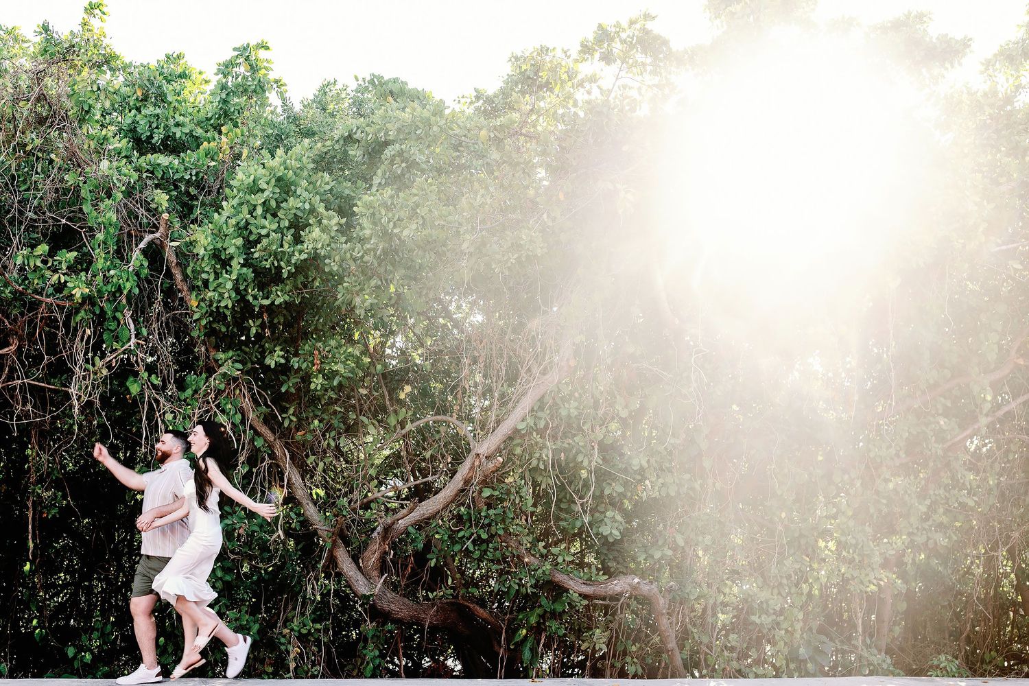 Alexia and Sam laugh together beneath sunlit tropical trees in Isla Mujeres.