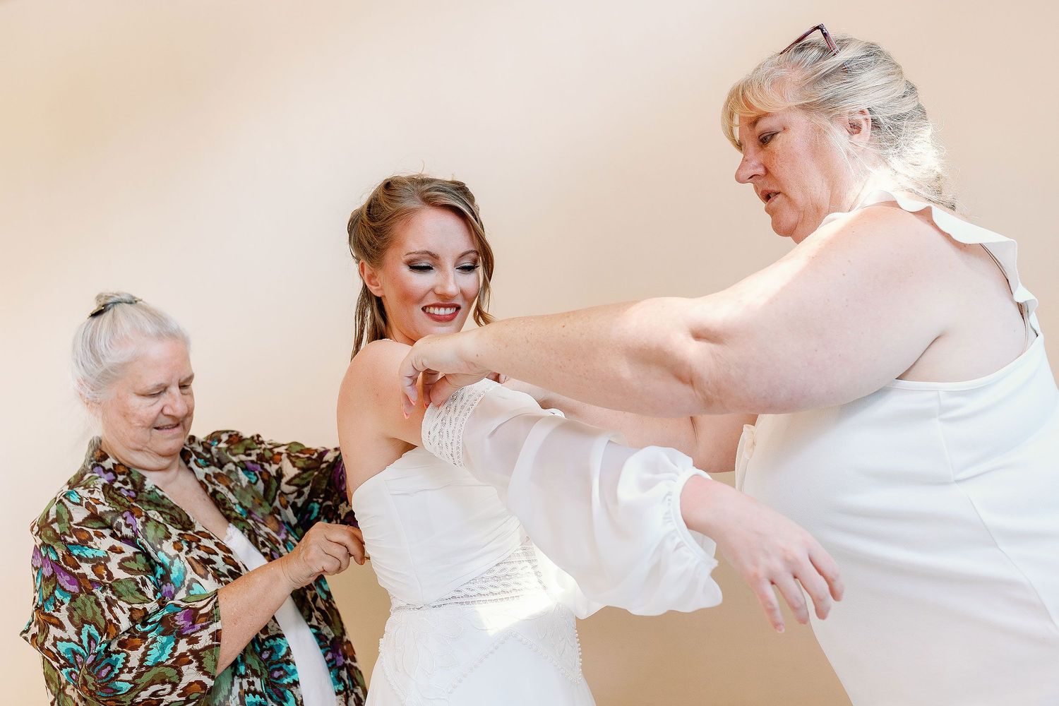 Nicole smiling as two women help her put on her wedding dress before her intimate Blue Venado wedding in Playa del Carmen.
