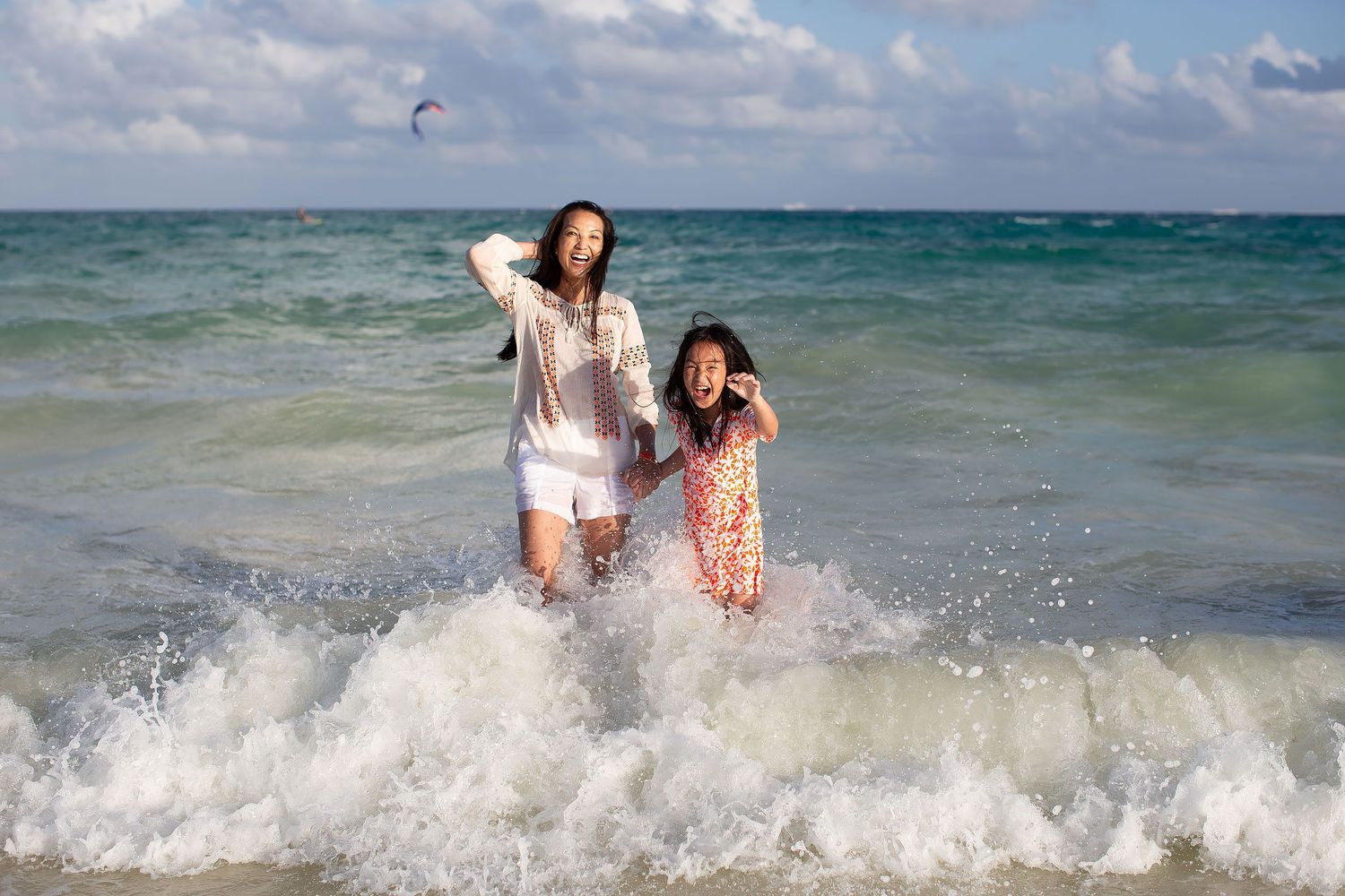 Mother and daughter wearing light coordinated beach outfits during a playful family photo session in Playa del Carmen, Riviera Maya.