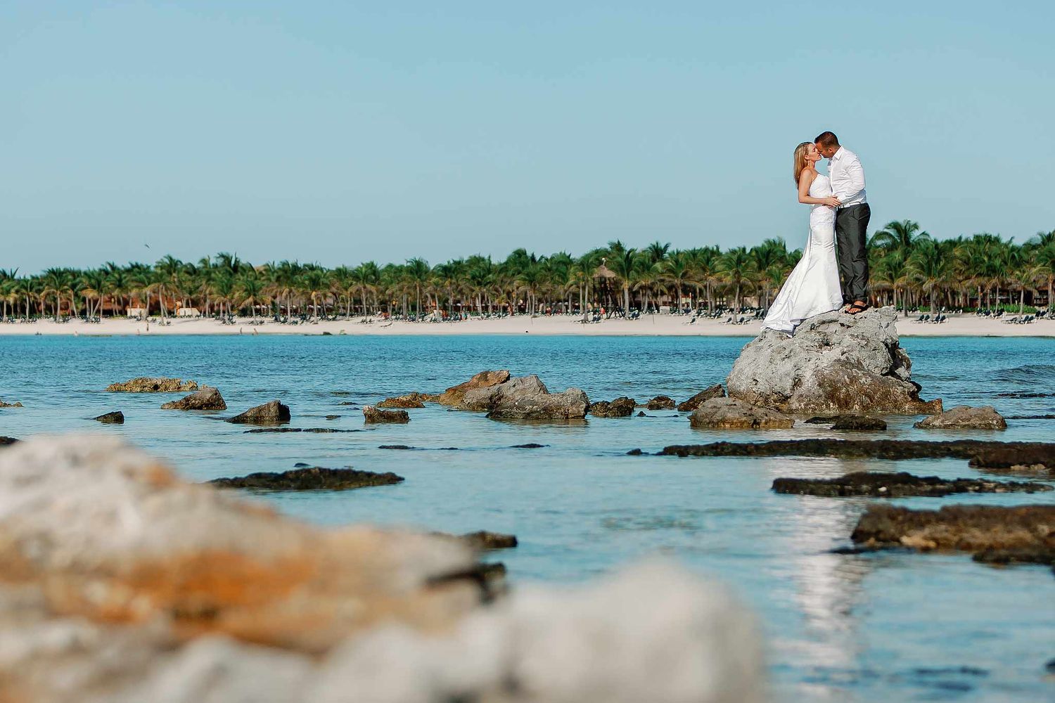 Bride and groom kissing on seaside rocks at Meliá Cozumel captured by a Cozumel wedding photographer with Caribbean beach views.
