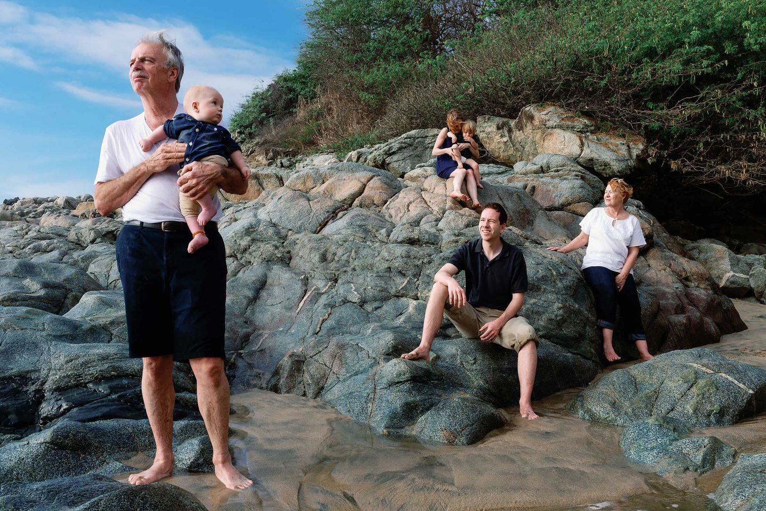 Multi-generation family wearing coordinated neutral beach outfits during a family photo session on the rocky coastline of Puerto Vallarta.