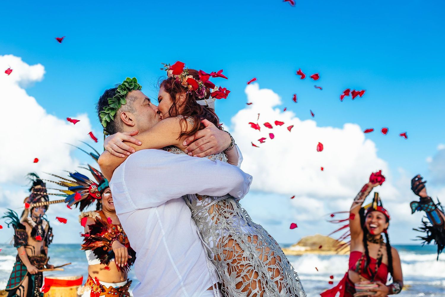Sarah and Evish kiss beneath falling red petals after their beach ceremony.
