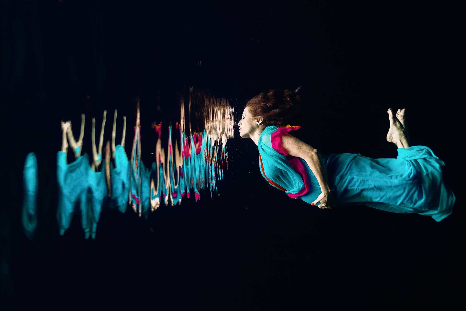 Pregnant woman floating underwater in a turquoise dress during a Riviera Maya underwater maternity photography session.