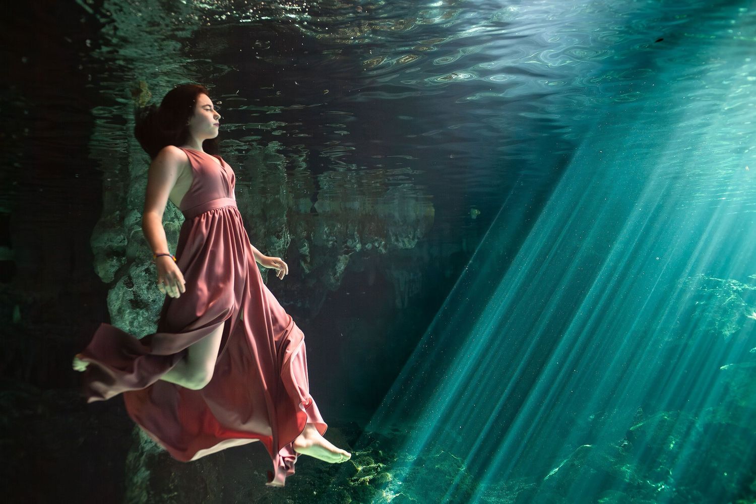 Underwater quinceañera portrait in a Tulum cenote with flowing dress, sun rays, crystal-clear water, and natural beauty.