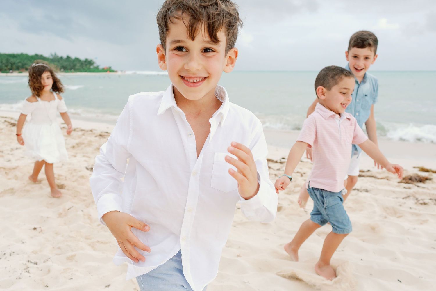Children wearing coordinated light beach outfits during a playful family photo session on the beach in Puerto Morelos, Riviera Maya.