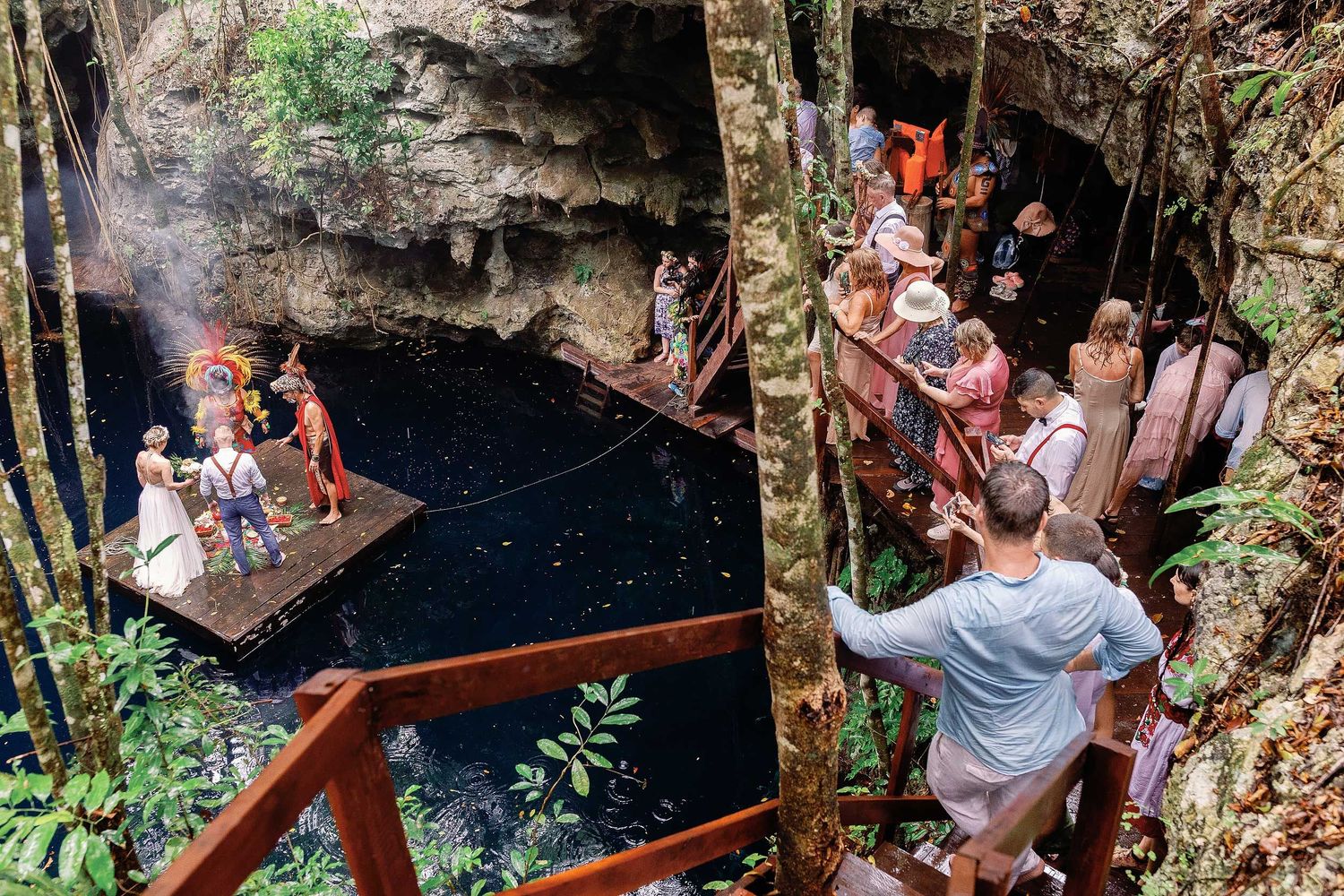 Wide view of Jeff and Veronica’s Maya wedding ceremony as guests watch from the wooden walkways surrounding Cenote Hats’uts.